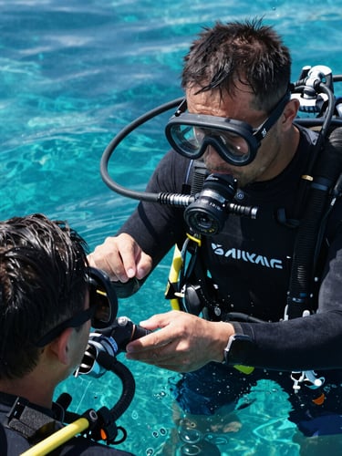A professional diving instructor demonstrating regulator recovery to a student in clear turquoise water, close-up, natural sunlight, high technical detail