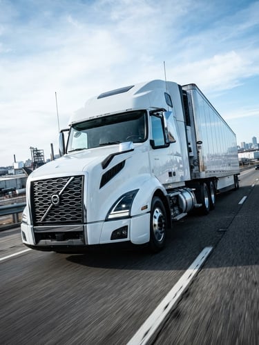 Low-angle powerful perspective of a modern clean freight truck on an open highway under crisp morning daylight, high-contrast cool-toned industrial lighting