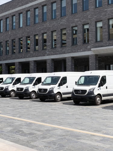 Wide environmental shot of branded white service trucks parked in clean formation outside a modern brick corporate office building, bright crisp morning daylight, slate grey tones, architectural framing