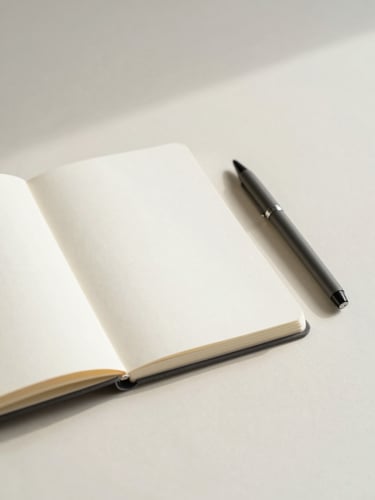 Minimalist workspace detail with an open notebook, a clean pen, and soft overcast daylight casting gentle shadows on a light cream surface