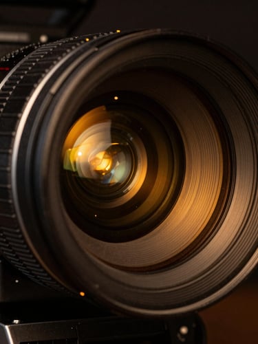 Macro close-up of a high-end cinema camera lens with glowing amber studio backlighting reflecting off the glass, anamorphic lens, 35mm.