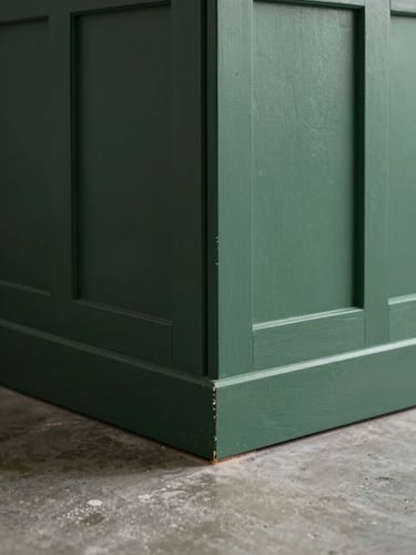 Close-up of a finished interior corner—dark green panelled wall meeting a polished concrete floor, precise joinery visible at the junction, cool north-light studio illumination emphasizing surface texture and geometric precision, no people