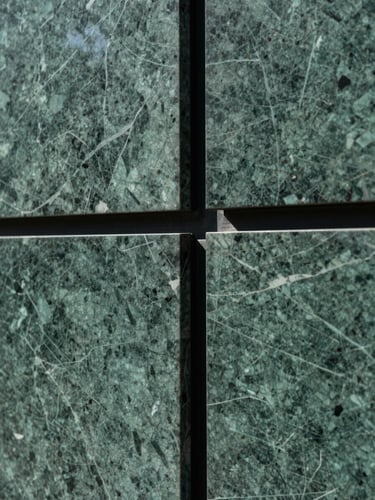 Close-up architectural detail of a deep-green marble wall panel meeting a polished black steel frame, precise joinery visible, cool diffused north light, no people, abstract material geometry