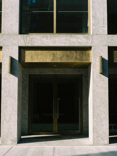 Straight-on architectural elevation of a modern building facade, sharp afternoon sunlight casting geometric shadows, raw concrete and brushed brass details, 35mm film photography.