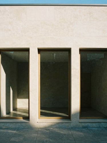 Straight-on elevation of a minimalist limestone building facade, sharp geometric shadows from strong afternoon daylight, raw oak window frames, architectural film photography, 35mm lens.
