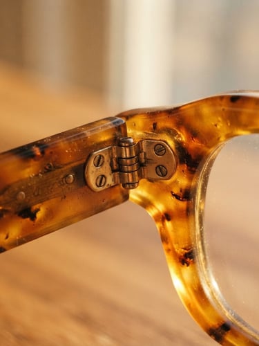 A macro close-up of thick, hand-polished amber acetate eyewear catching warm golden hour window light, showing the rich tactile texture and heavy frame joints, 35mm photography.