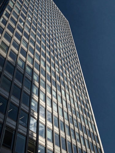 Wide panoramic shot of a glass high-rise financial district tower facade, left-framed, cool north-facing daylight reflecting on polished steel and glass curtain walls, geometric grid of windows receding upward, deep navy sky above, minimal and architectural