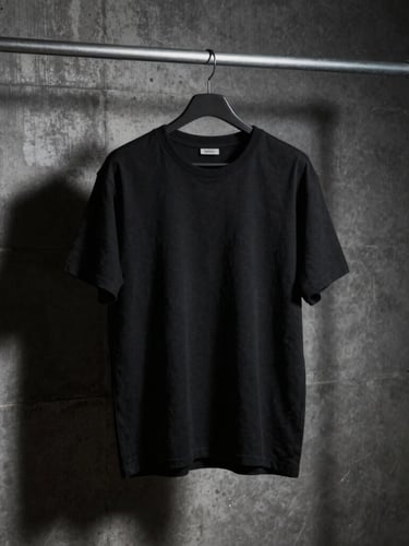 A heavy-weight cotton black t-shirt hanging on an industrial steel rack against a raw concrete wall, moody directional lighting, deep shadows