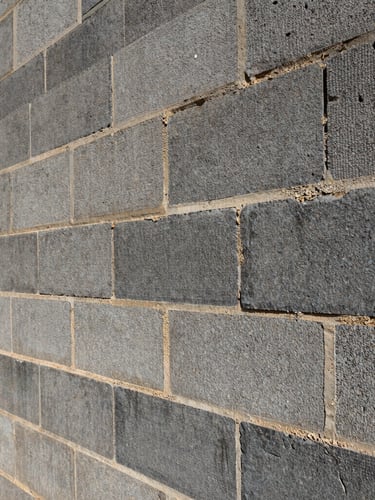 Low-angle heroic shot of a massive structural CMU block wall under hard, high-contrast natural sunlight, sharp focus, 35mm lens