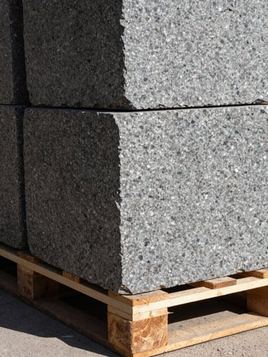 High-contrast close-up of raw, hand-dressed granite blocks stacked on heavy timber pallets, hard natural sunlight casting deep shadows on the rough slate-gray stone textures.