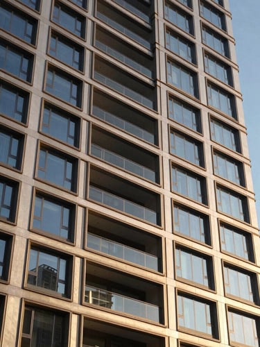Tight abstract architectural angle of a luxury residential building facade, warm champagne accents, sharp shadows from late-afternoon sun