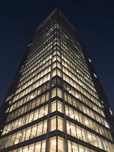 Sharp architectural twilight photography of a modern steel-and-glass Gurgaon office tower, deep navy sky, warm champagne interior lights reflecting on glass, wide-angle symmetrical shot