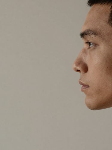 Minimalist studio portrait of a male designer, side profile, warm clay-toned lighting, soft diffused drop shadows, neutral desaturated background, sharp macro lens composition.