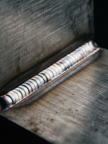 Macro shot of a flawless TIG weld joint on brushed steel, sharp focus, dramatic side lighting, industrial minimalist editorial style