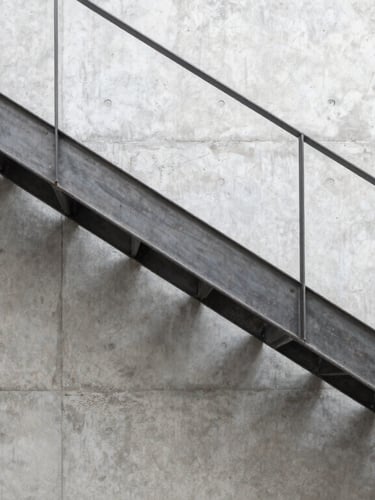 Wide architectural shot of a minimalist steel staircase installed in a modern concrete residence, clean joints, natural side light, industrial editorial style