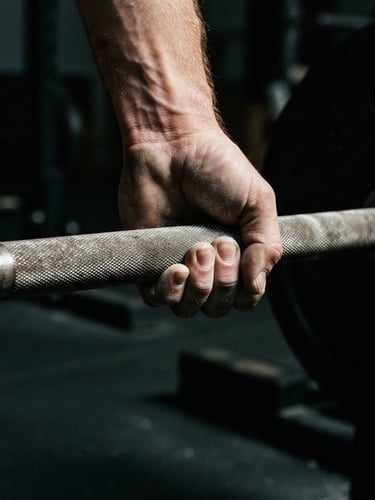 High-contrast editorial photograph of hands gripping a knurled barbell, dramatic side-lighting, deep shadows, sharp focus on raw steel texture, 35mm