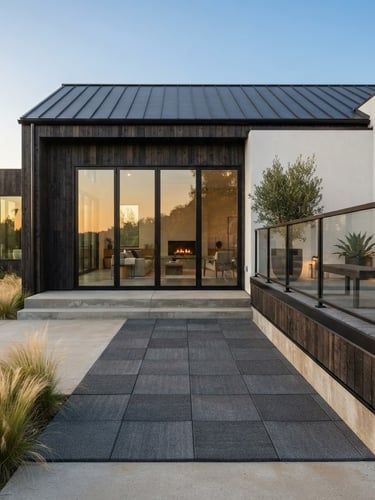 Wide architectural elevation of a modern home exterior at golden hour, showing a section of interlocking rubber deck tiles seamlessly integrated with the building's foundation, sharp focus on the material texture and clean lines, high-contrast natural daylight, to the right third of the frame.