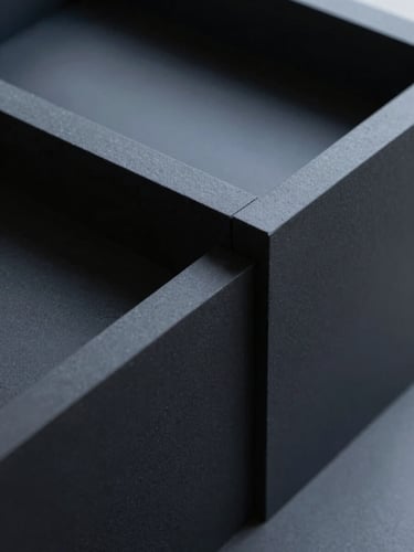 Minimalist close-up of a matte black architectural model with precise geometric lines under sharp, cool daylight shadows, 35mm