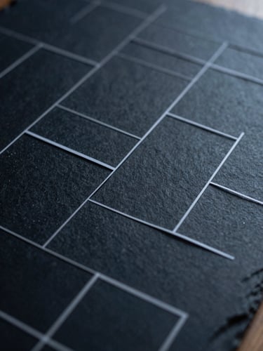 Macro close-up of structured paper wireframes on a dark slate desk, cold morning light, sharp geometric shadows.