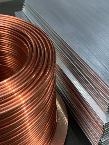 Close-up of shiny copper wire coils and clean sorted aluminum sheets in an industrial setting, bright natural daylight