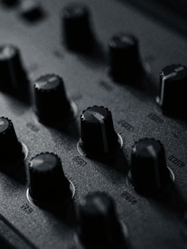 Extreme close-up of vintage synthesizer knobs, low-key chiaroscuro lighting, desaturated monochrome with cold blue undertones, grainy 35mm film