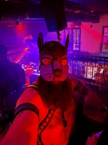 Man in a pup mask and bare chest taking a selfie in a club.