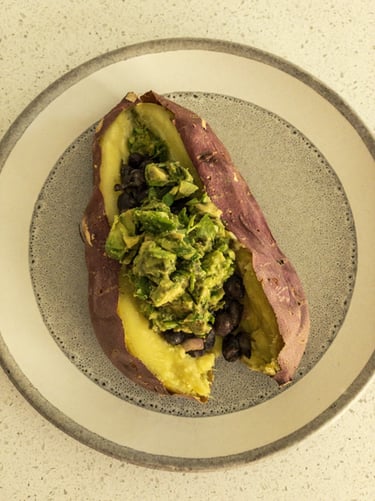 Loaded baked sweet potato topped with black beans and chunky green guacamole, served on a speckled c