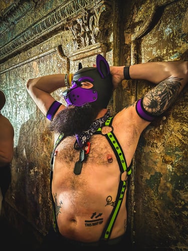 Shirtless man in pup mask, leaning against a bar wall