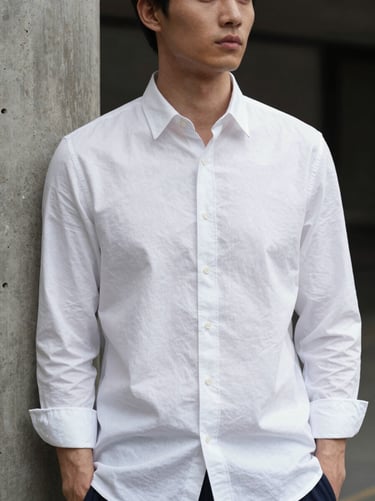 Portrait of a model in a crisp white organic cotton poplin shirt with structured cuffs, standing near a concrete column