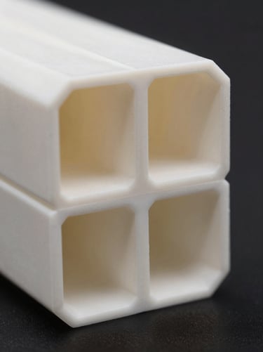 Macro close-up of a structural PVC extrusion cross-section, showing clean geometric chambers and precise wall thickness, high-contrast studio lighting.