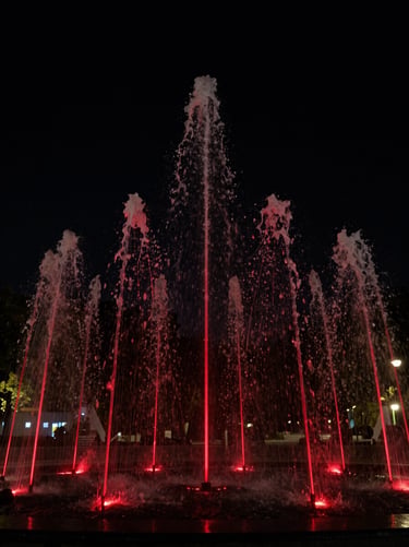Low-key architectural photography of a modern outdoor water fountain at night, sharp red laser lines reflecting off cascading water, deep black background