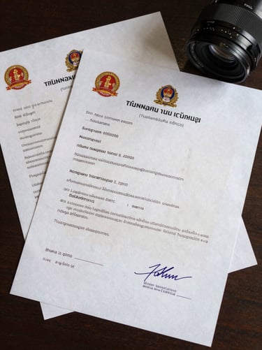 Close overhead shot of official Thai film permit documents spread on a desk, government stamps and signatures visible, even studio lighting, no faces