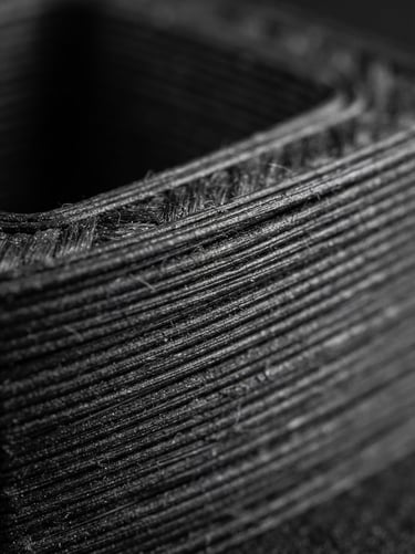 Extreme macro close-up of pristine layer lines on a dark carbon-fiber nylon printed part, high-contrast studio lighting, sharp depth of field, 50mm lens.