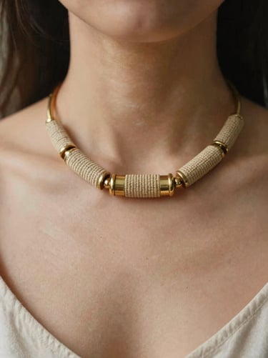 Portrait close-up of an elegant statement necklace combining hand-woven textile cylinders with polished brass elements, shallow depth of field