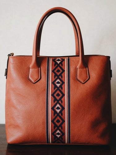 Portrait shot of a structured terracotta leather handbag with a bold geometric tenun accent strip down the center, warm editorial lighting