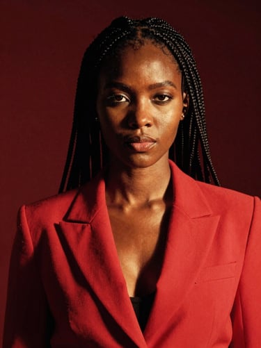 Editorial portrait of a Kenyan woman with braided hair, wearing a structured red blazer, high-contrast studio lighting with rich deep shadows, bold and confident expression.