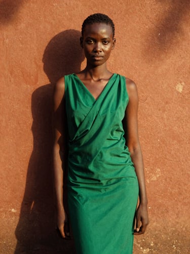 Medium-shot of a Kenyan female model in a vibrant emerald green draped dress, standing against a textured terracotta wall in Nairobi, dramatic high-contrast shadows, warm golden lighting.