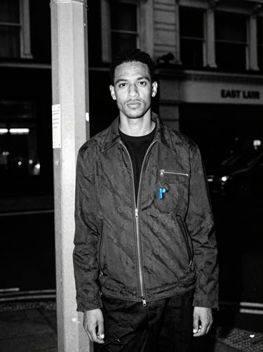 Environmental portrait of a fashion commentator on an East London street corner, harsh direct flash, high-contrast monochrome with electric blue accents.