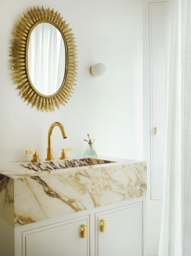 Salle de bain de luxe avec miroir soleil, robinetterie en laiton doré et vasque en marbre Calacatta