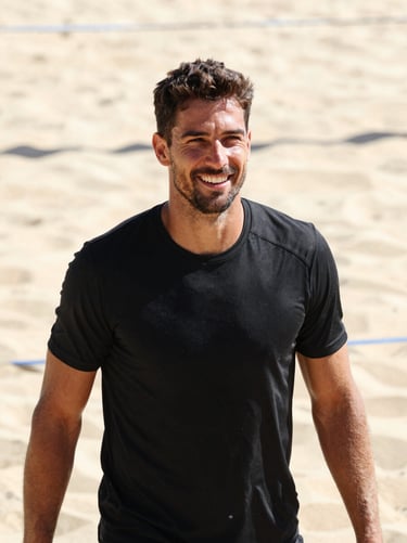High-contrast portrait of a male beach volleyball coach smiling, sun-drenched sand background, bright outdoor sunlight, 35mm