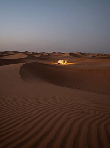Cinematic wide-angle shot of vast sand dunes in Dubai at twilight, deep shadows, a single low-angle warm light from a private desert camp.