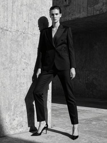 High-contrast black and white fashion editorial, model posing against a brutalist concrete architectural backdrop, hard directional sunlight, deep sharp shadows