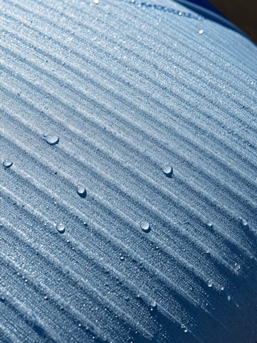 Macro shot of the crisp ice-blue evaporative weave texture, water droplets bead-blasting off the fabric under bright high-contrast sunlight, sharp 35mm detail