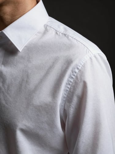 Close-up of a crisp white cotton dress shirt collar and structured shoulder seam, soft elegant shadow, high-contrast dark background