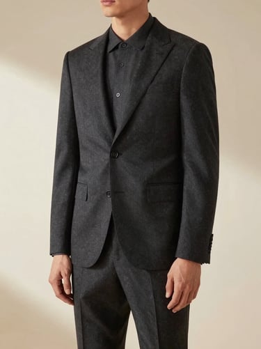 Editorial fashion photography of a man in a sharp, structured 2-piece tailored suit, deep charcoal tones, soft natural directional light