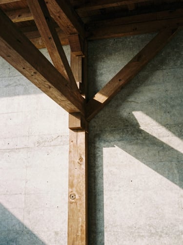Architectural detail of an industrial loft showing heavy timber beams meeting a raw concrete wall, sharp side daylight.