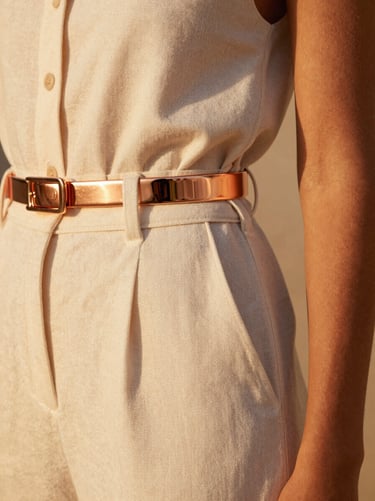 Close-up of high-end cream linen resort clothing on a model, warm golden hour light reflecting off polished rose-gold hardware details, soft shadows