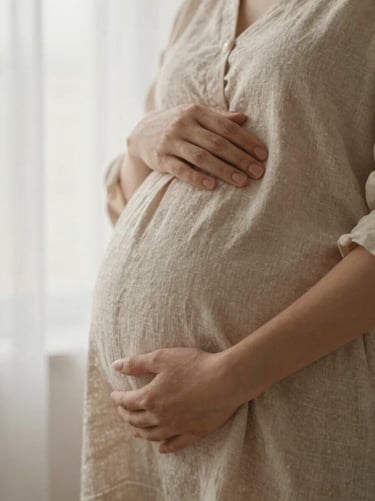 Close-up of a pregnant mother's hands gently resting on her belly, soft linen textures, warm window light, editorial feel