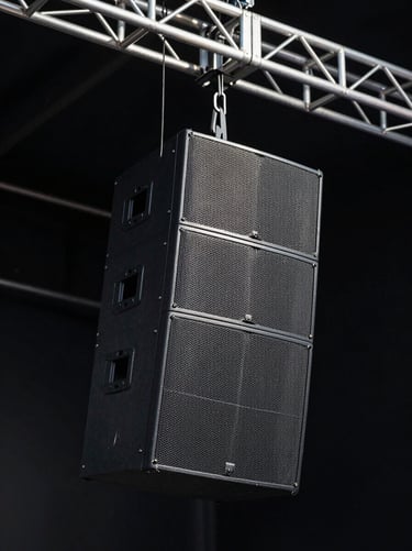 Pristine professional line-array sound system suspended from a massive aluminum truss, dark background with dramatic stage light, high contrast.