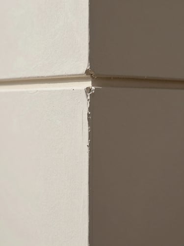 Portrait close-up of a finished gypsum wall corner, perfectly square joint, smooth skimmed surface under soft north-facing daylight, no people, tight architectural framing